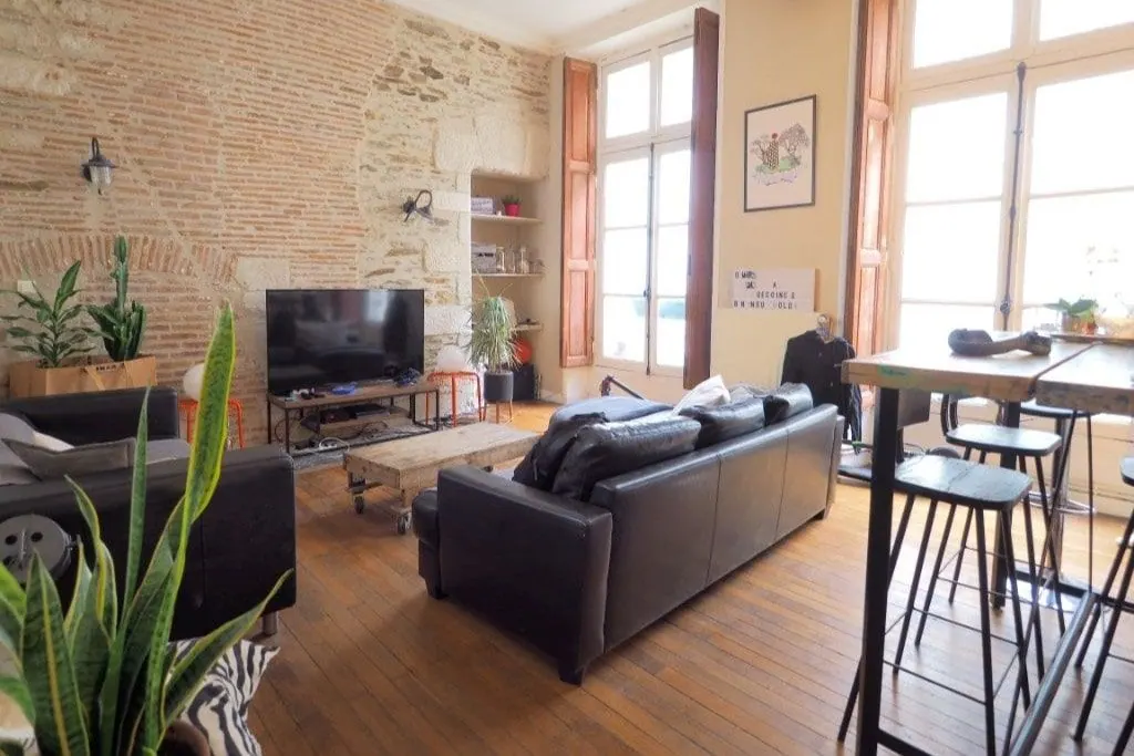 Salon lumineux d’un appartement ancien avec murs en pierre apparente et grandes fenêtres