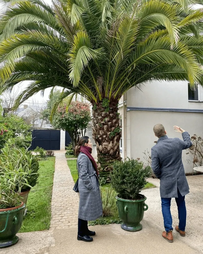 Deux clients visitant un jardin avec un palmier devant une maison